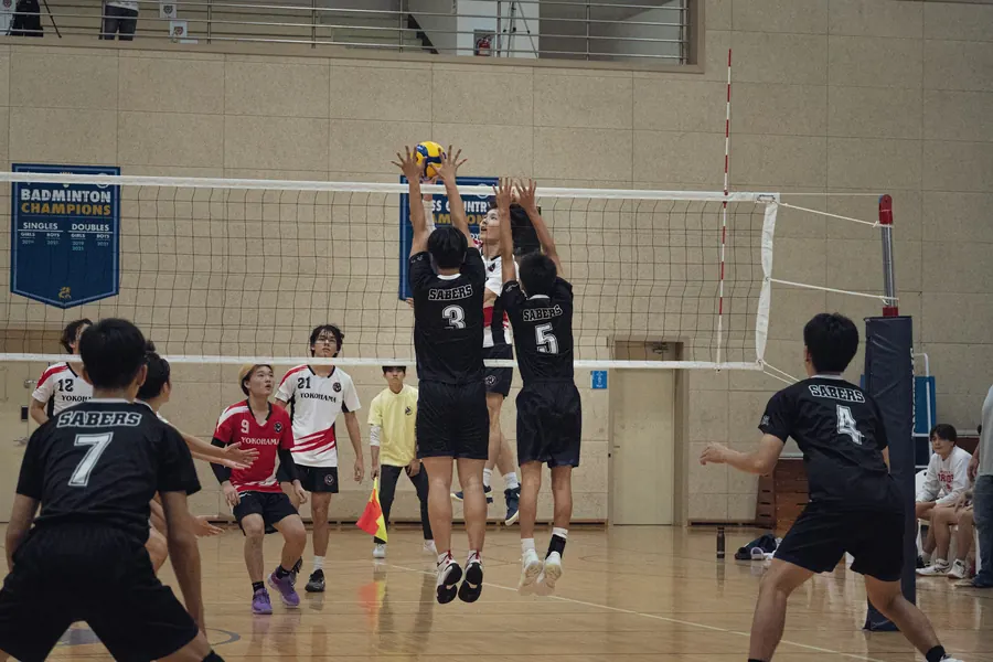A boys team jumping to block at the net, seen from behind the back row
