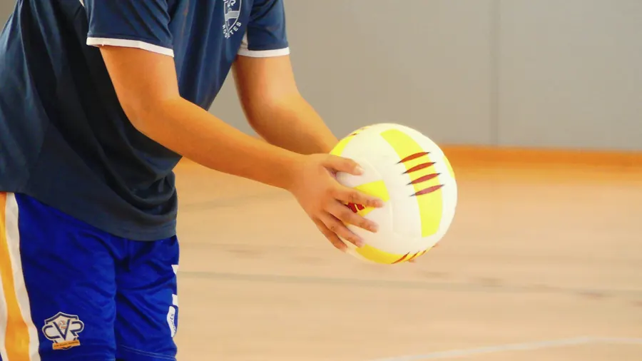 A player in a navy shirt holds a volleyball at their hip, ready to serve