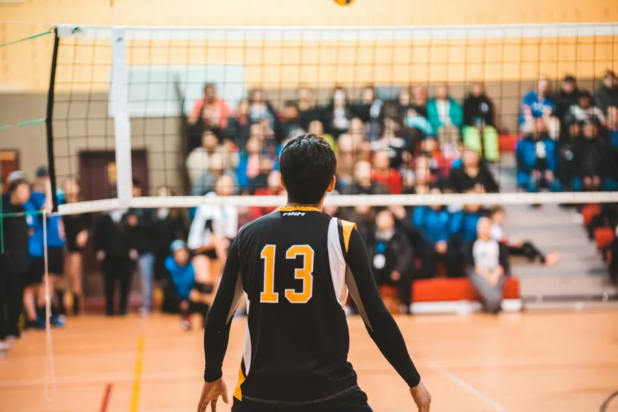 A player in a black number 13 jersey, seen from behind, watches the court during a crowded tournament